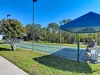 Tennis court with shaded seating area surrounded by lush landscaping under bright blue skies.