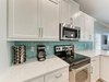 Whip up your favorite meals in this bright kitchen featuring stainless steel appliances, elegant white cabinetry, and coastal-inspired teal backsplash that adds a refreshing pop of color.
