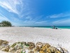 Pristine white sand beach stretches along turquoise waters under dramatic blue skies with wispy clouds.