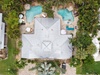 Aerial view of a tropical vacation home featuring a winding pool, thatched-roof cabanas, and lush palm gardens surrounding the property.