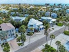 Aerial view of a coastal neighborhood with tropical homes, palm trees, and turquoise waters in the distance.