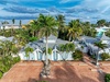 Aerial view of tropical rental property featuring white buildings with blue accents surrounded by lush palm trees and tropical landscaping in a peaceful residential setting.
