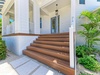 Elegant wooden steps lead to your covered porch entrance, surrounded by lush tropical palms and pristine white columns.