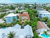Aerial view of a vibrant coastal neighborhood featuring tropical palm trees, colorful vacation homes with private pools, and bay access. Situated in a quiet residential area steps from the waterfront.