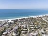 Aerial view of coastal community with pristine white sand beach and turquoise waters, featuring residential neighborhood just steps from the shore.