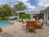 Your private poolside retreat features mid-century modern seating under a chic umbrella, surrounded by swaying palms and lush tropical greenery—perfect for lazy afternoons in the sun.