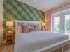 Sink into your plush bed surrounded by tropical-inspired style and warm lighting. Step through the patio doors to your private outdoor space or relax beneath soft, breezy curtains and chic greenery-patterned walls.