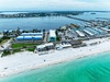 Aerial view of a beachfront property situated between pristine turquoise waters and a bay marina, showcasing a tranquil waterfront location with white sand beaches and coastal charm.