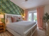 Drift off beneath soft linens and a ceiling fan as natural light fills your tranquil retreat, where tropical wallpaper and blush tones meet plush comfort.
