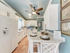 Your coastal kitchen awaits with crisp white cabinetry, modern appliances, and a cozy island perfect for morning coffee or evening conversations under the warm ceiling fan glow.