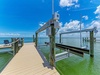 Private boat dock with boat lift on expansive waterfront, featuring turquoise waters, sunny skies, and relaxing Adirondack chairs for waterside lounging.