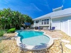 A private backyard retreat featuring an inviting pool with tropical landscaping, spacious patio areas, and coastal-style architecture under clear blue skies.