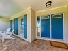 A welcoming covered porch with elegant blue double doors, classic shutters, brick pavers, and cozy white Adirondack chairs invite relaxation at your vacation retreat.