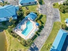 Aerial view of tropical resort featuring turquoise pool area surrounded by palm trees and blue-roofed buildings.