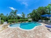 Tropical backyard oasis framed by swaying palms and lush greenery, ideal for sunny afternoons by the sparkling pool and outdoor dining under the blue umbrella.
