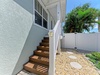 Coastal-style vacation home exterior featuring a clean facade, private entrance, and tropical landscaping with lush palm trees and a charming pebble pathway leading to your getaway.