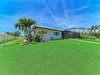 Single-story vacation home featuring a screened patio and lush tropical landscaping with palm trees, set in a sunny Florida neighborhood with expansive lawn space.