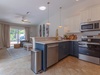 Step into your bright, beachy haven featuring a fully equipped kitchen with modern appliances, coastal pendant lighting, and an open flow into the living area where tropical décor sets the mood for relaxation.
