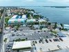 Aerial view of a waterfront vacation rental property featuring colorful buildings, private boat docks, and parking, situated along a scenic coastal bay with easy access to local amenities.