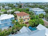 Aerial view of a tropical waterfront neighborhood with lush palm trees, colorful homes, and a private pool nestled in a vibrant coastal community near the water.