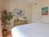 Slip into crisp linens in your serene bedroom, where coastal artwork and lush greenery create a tranquil retreat after exploring nearby beaches and attractions.
