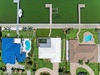Aerial view reveals three waterfront properties with private boat docks, pools, and lush landscaping along a calm green waterway.