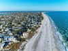Aerial view of a pristine beachfront community with crystal-clear turquoise waters and white sandy shores stretching along the coastline.