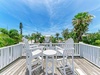 Coastal deck with white Adirondack chairs overlooks tropical palms and ocean, offering a peaceful retreat with scenic views and blue skies above.
