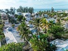 Aerial view of tropical beachfront community with palm trees and colorful homes near pristine coastline.