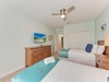 Your serene bedroom retreat features two plush beds with crisp linens, a ceiling fan for comfort, and coastal artwork reminding you that relaxation awaits just outside.