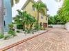 Sunny yellow three-story property nestled among lush palms, with convenient brick paver parking and tropical landscaping framing the entrance.
