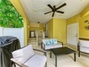 Your covered patio offers a breezy retreat with comfortable seating, a ceiling fan, and vibrant tropical greenery just beyond the gate—perfect for lounging or grilling outdoors.