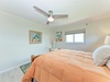 Slip into this serene bedroom with soft coral linens and coastal artwork, where a ceiling fan keeps you cool and peaceful beach vibes welcome you to unwind.