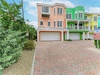 Colorful townhomes line a quiet street with parking and lush tropical greenery marking the entrance to the property.
