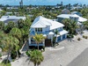 Stunning aerial view of a coastal beach house surrounded by palm trees in a tropical island community.
