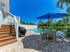 This bright Florida-style backyard features a private pool, shaded dining beneath a blue umbrella, and a BBQ grill—perfect for relaxed outdoor living and entertaining under sunny skies.