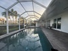 Your private screened pool catches the warm afternoon light beneath its vaulted enclosure, with loungers ready for relaxation and tropical palms swaying just beyond the pristine lawn.