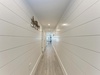 Walk through this bright hallway with crisp white shiplap walls and gleaming hardwood floors that lead to your spacious living areas ahead.