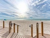 Pristine white sand beach with wooden boardwalk access, featuring expansive shoreline under dramatic cloudy skies.