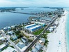Aerial view captures a stunning coastal town with pristine beaches, calm turquoise waters, and charming vacation properties lining both the beachfront and bay side waterways.