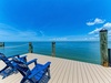 Waterfront dock with vibrant blue chairs overlooking endless turquoise waters under clear skies—perfect for morning coffee or sunset cocktails in your private oasis.