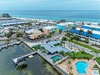 Aerial view of the beachfront resort area featuring colorful buildings, twin pools, marina access with boat docks, and pristine turquoise Gulf waters just steps away.