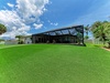 A modern tropical property featuring expansive lawn space, elegant covered patio, and lush palm landscaping under vibrant Florida skies, offering a private retreat for outdoor relaxation and gatherings.