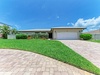 Beautifully landscaped home in a peaceful neighborhood with manicured lawn, palm trees, and paver driveway under sunny skies.