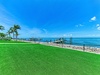 Waterfront property featuring private boat docks, palm trees, and expansive lawn area with direct access to pristine turquoise waters under clear blue skies.