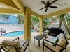 Picture yourself lounging in this covered patio, ceiling fan gently cooling you as you gaze at the sparkling pool. Comfortable seating invites you to unwind, with tropical palms framing your private backyard oasis.