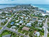 Aerial view of a coastal neighborhood featuring residential homes, palm-lined streets, waterfront access, and pristine white sand beaches along turquoise waters.