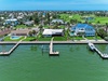 Aerial view of waterfront properties with private docks, lush lawns, and a golf course in a palm-lined coastal community under clear skies.