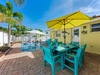Dine al fresco at your vibrant turquoise table while the pool sparkles nearby, shaded by tropical palms and a sunny umbrella.