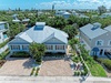 Aerial view of a charming coastal vacation home nestled in a lush tropical neighborhood with palm trees and nearby waterfront community amenities.